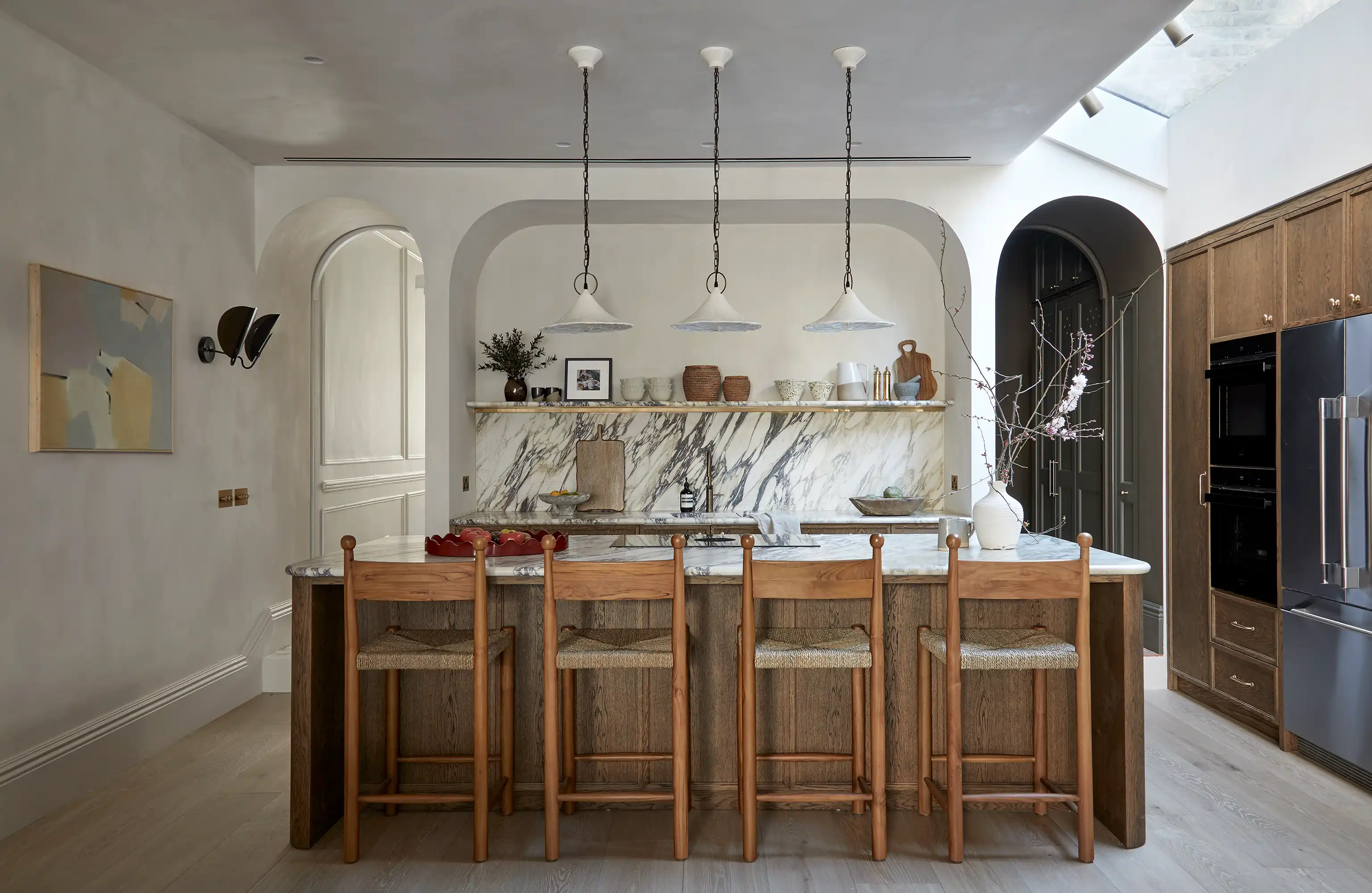 A modern kitchen featuring a marble island with wooden stools, stylish pendant lights, and elegant decor on the shelves.