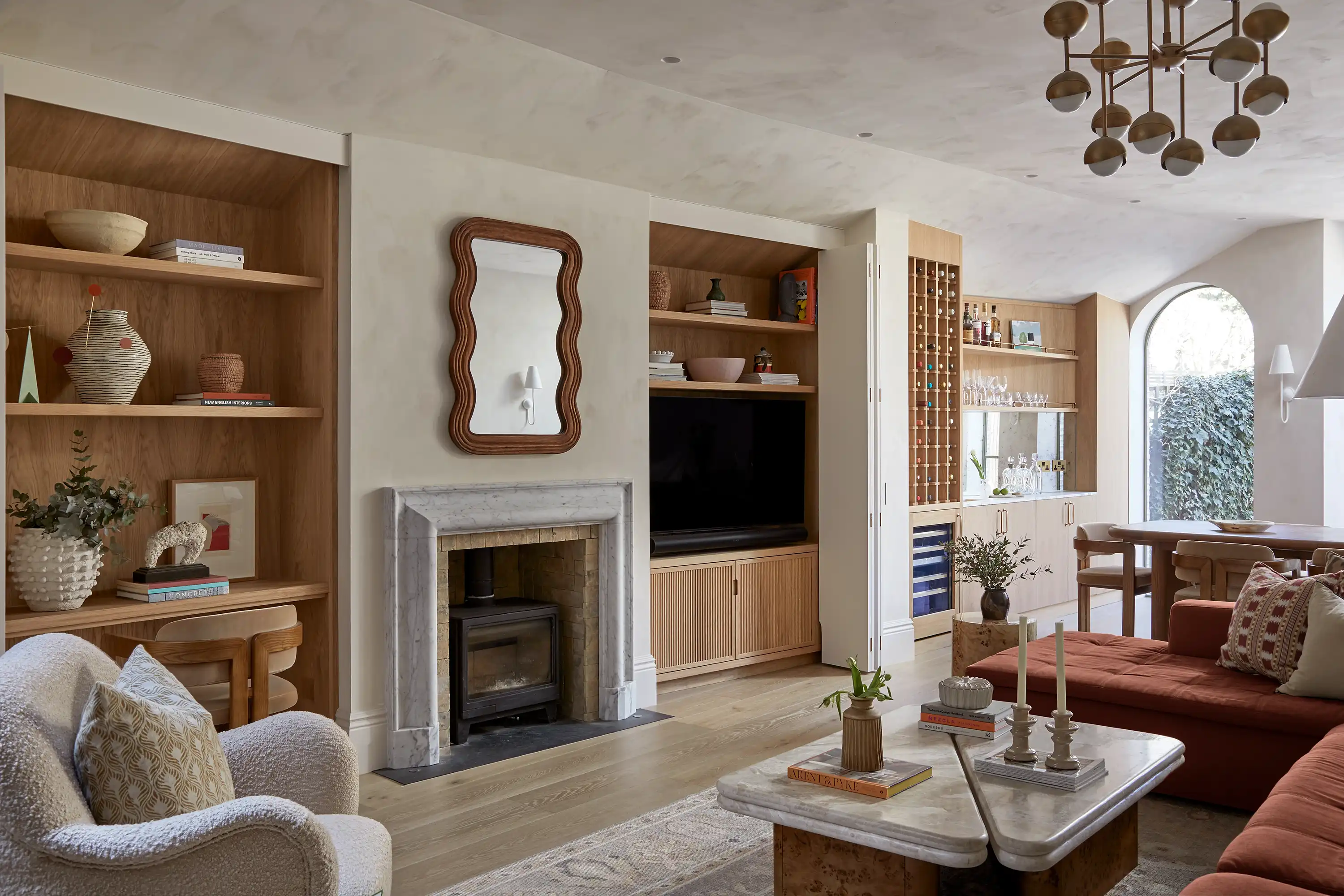 Cozy living room featuring a stone fireplace, shelf decor, a large TV, and modern furniture in neutral tones. Bright, inviting atmosphere.