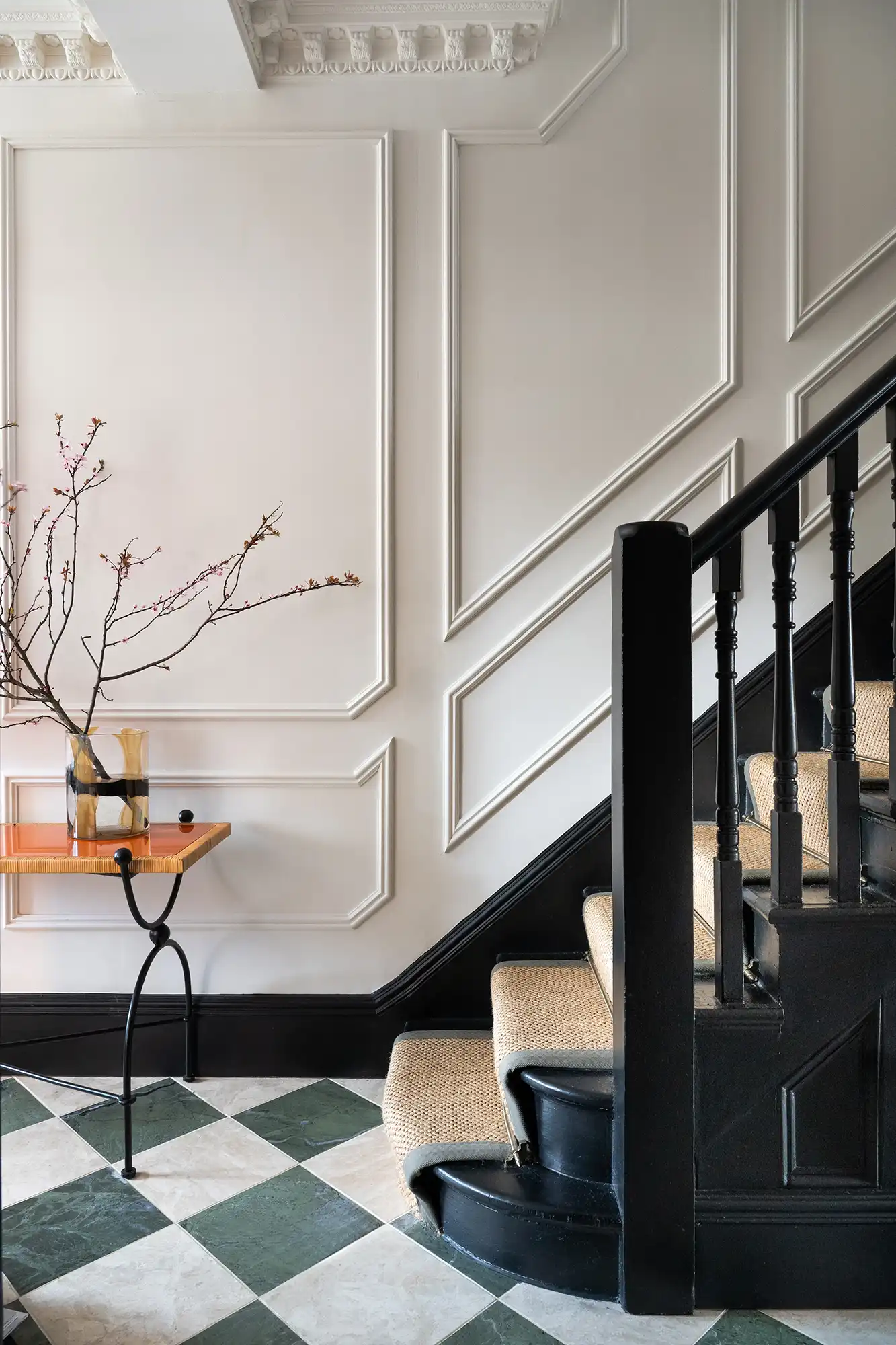 Elegant staircase with a textured wall, checkered floor, and a small table with a floral arrangement in a modern interior setting.